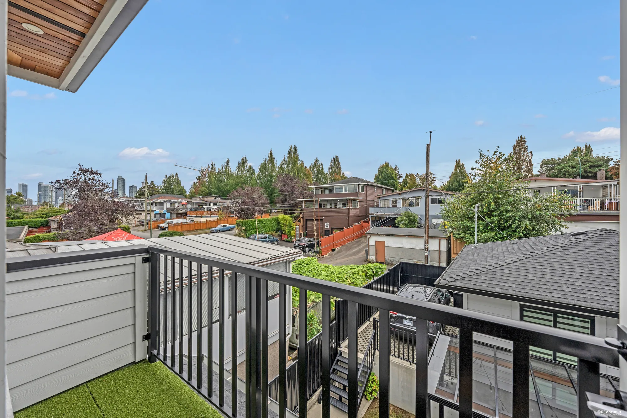 From the balcony: the garage roof and the lane below, rooftops and trees, the towers of downtown Vancouver on the horizon under a blue sky