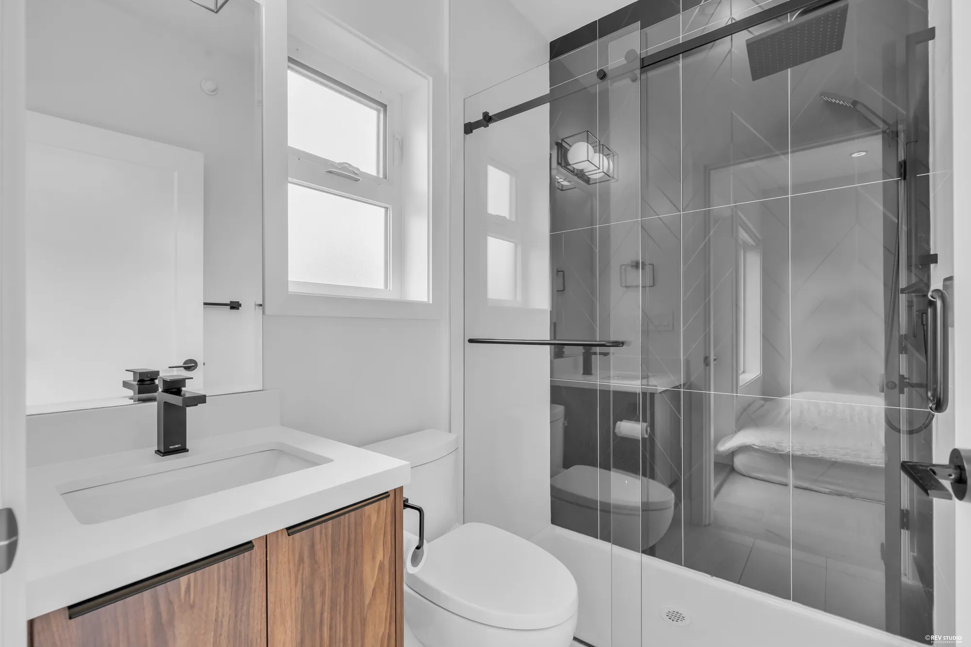 A bathroom with a glass shower in grey tile and a walnut vanity