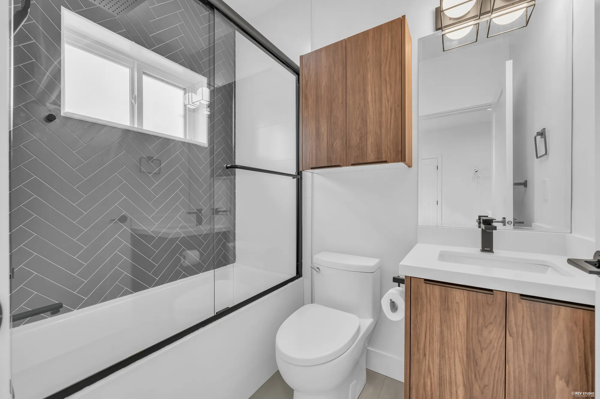 The hall bathroom: a tub and shower in dark herringbone tile behind a glass screen, a walnut vanity