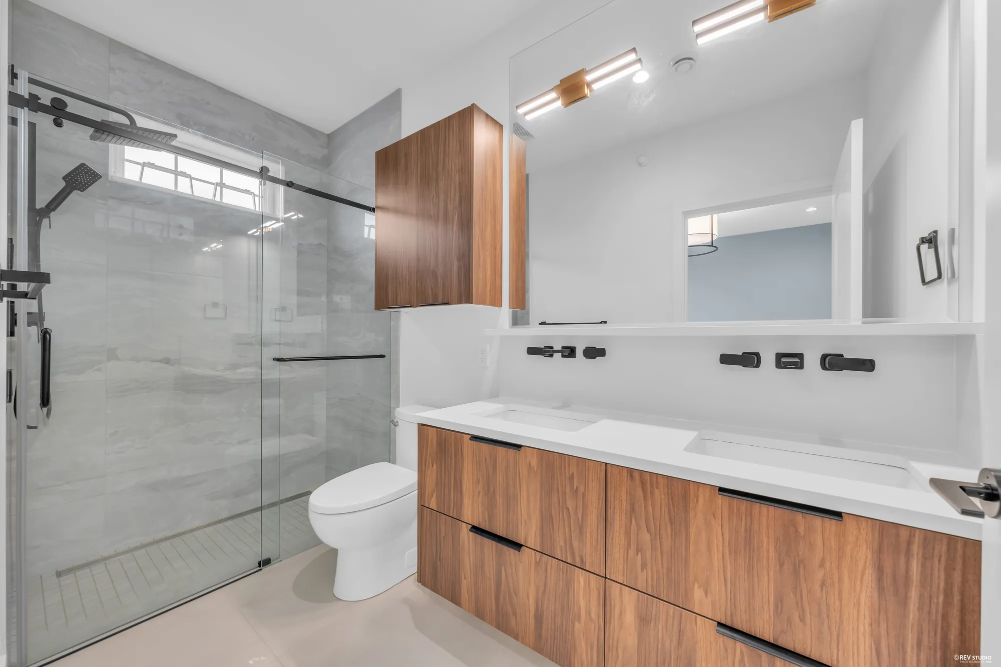 The primary bathroom: a double vanity in walnut with black taps, a glass shower in pale grey tile