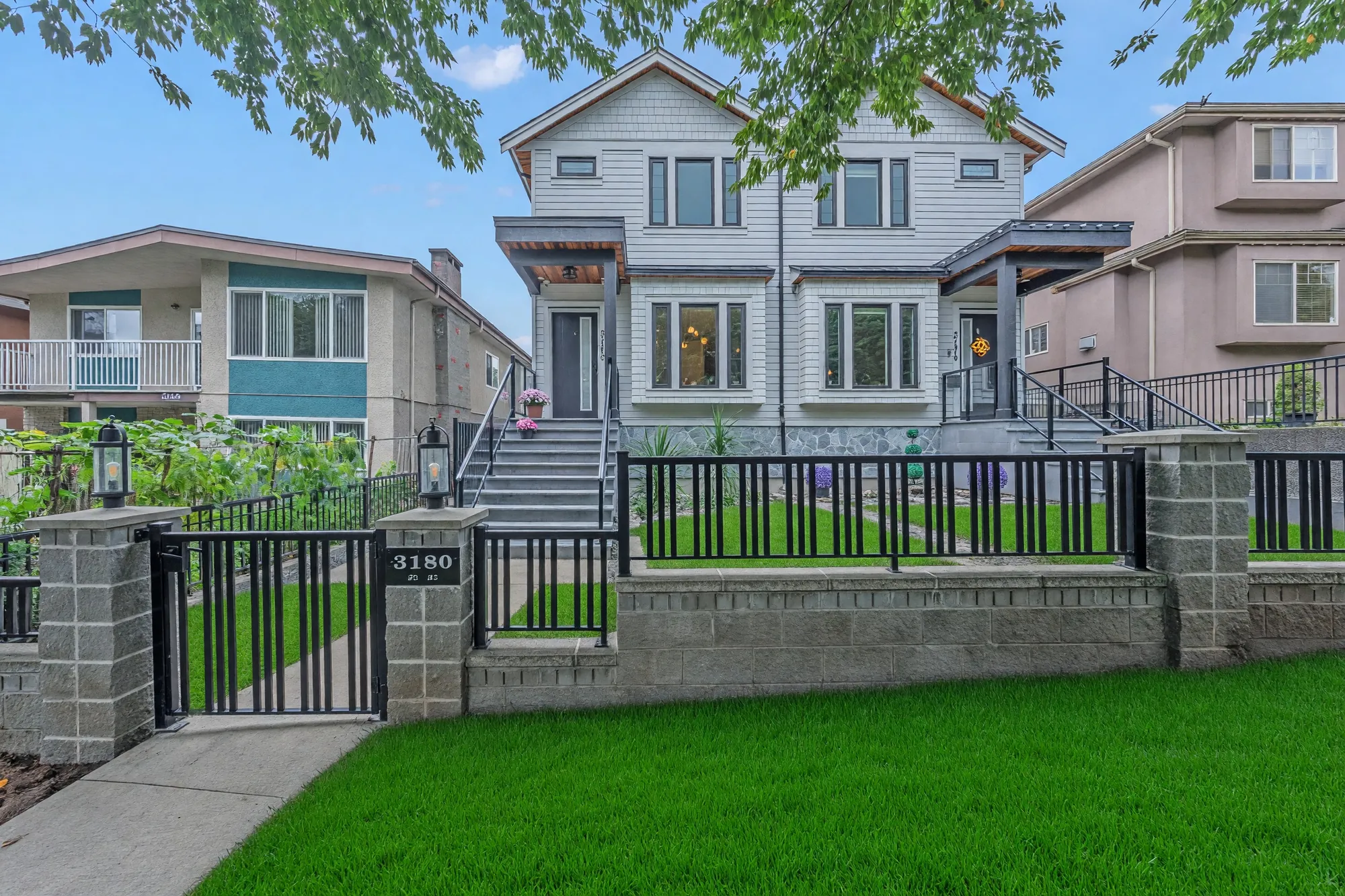 The gate and the low block wall from the sidewalk, the number 3180 on the gate post, both halves of the building and the neighbours behind