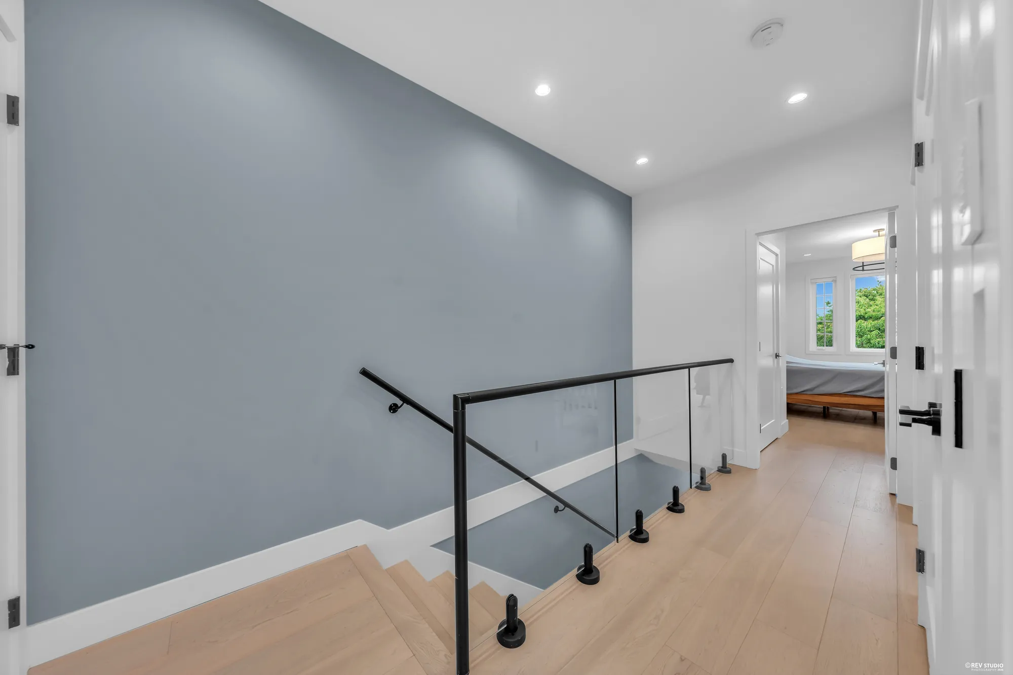 The upper hall with a glass stair rail, a blue-grey wall and a bedroom door ahead
