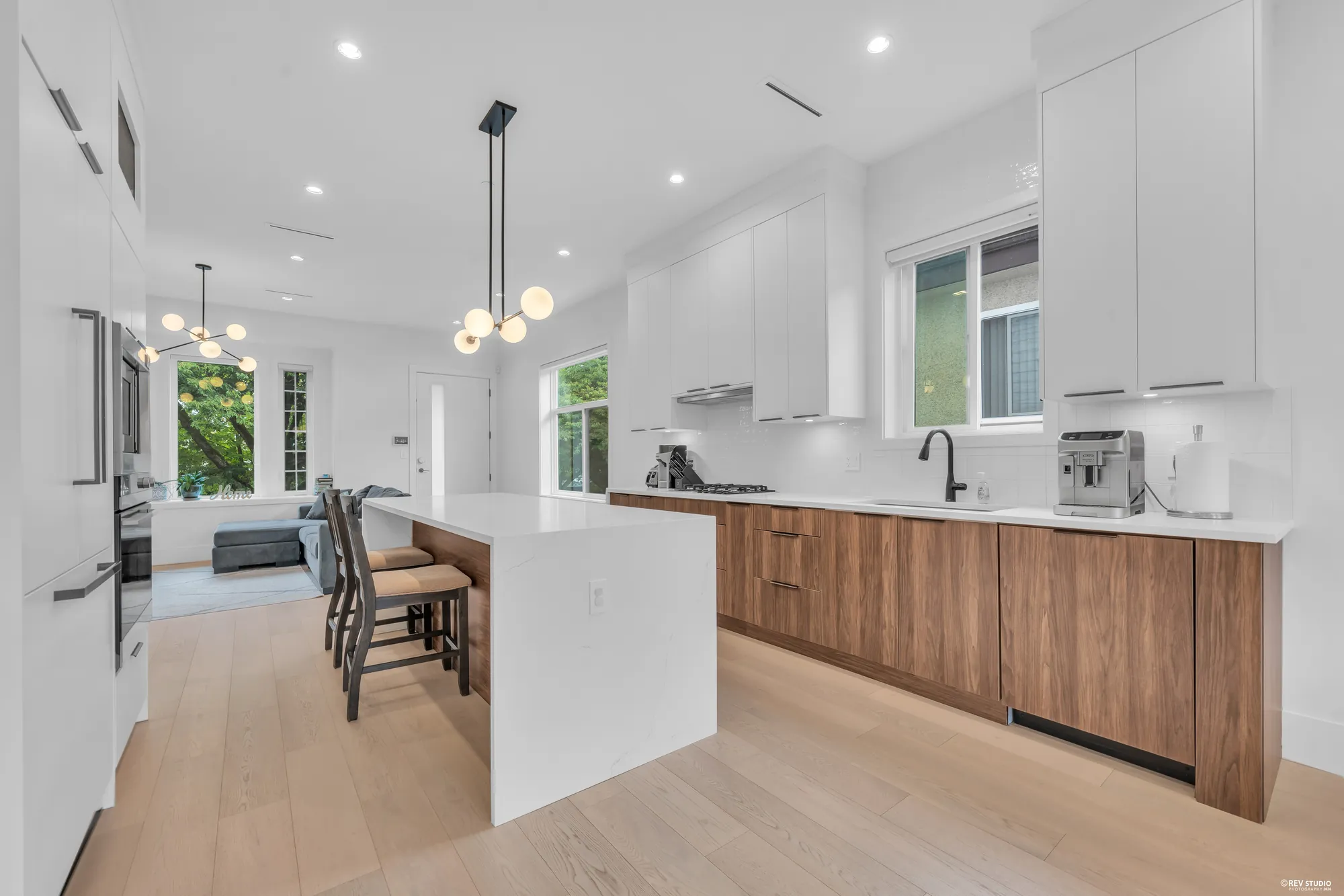 The kitchen: an island with a waterfall quartz top, walnut-toned lower cabinets and white uppers, three globe pendants, the dining room beyond