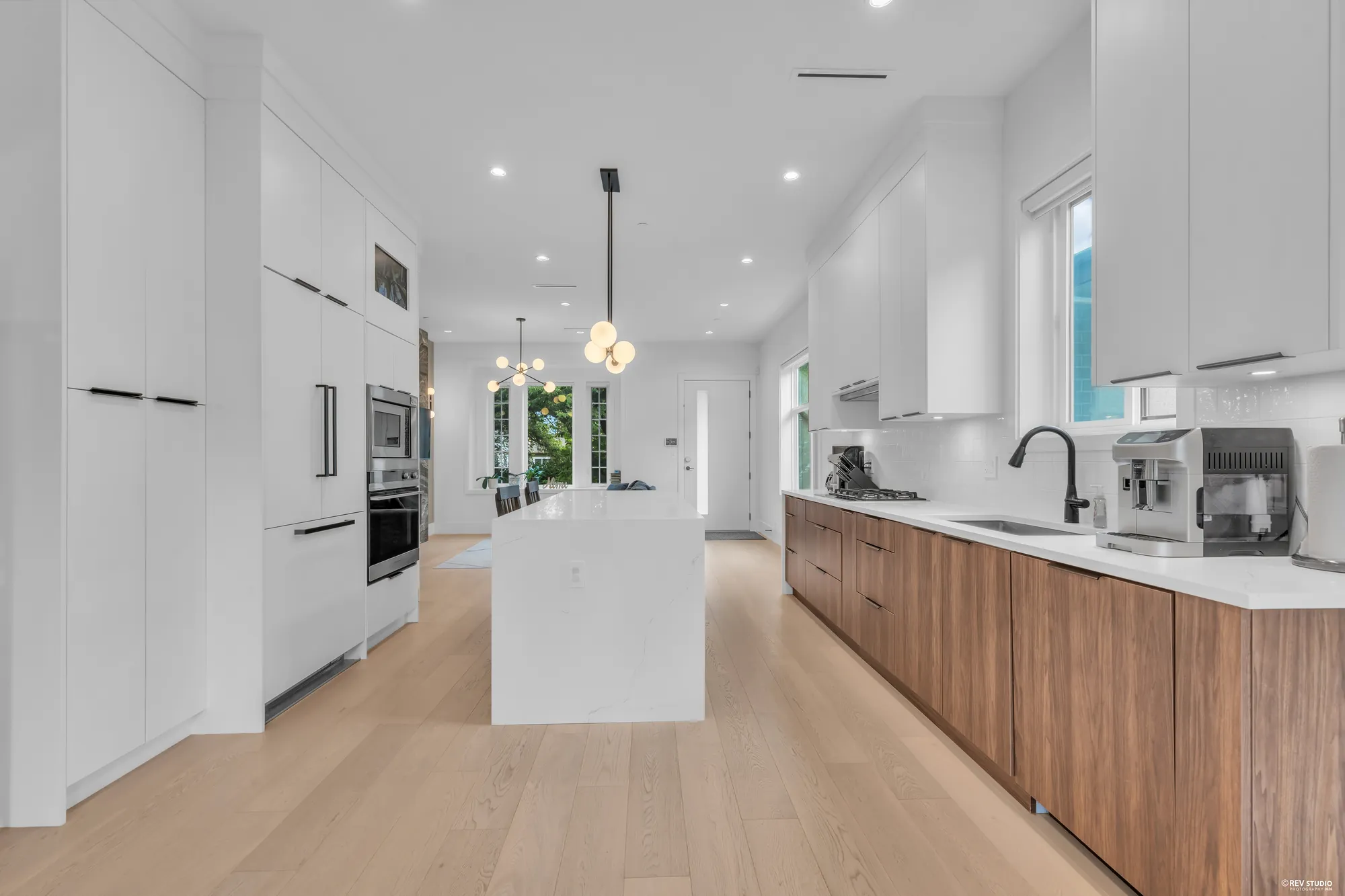 The kitchen along its length: tall white cabinets on the left, the island, the counter and a window on the right