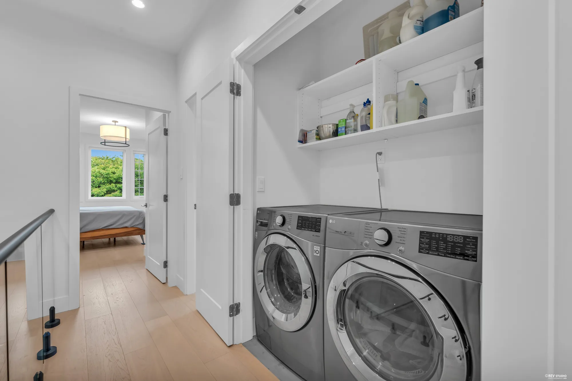 The laundry closet in the upper hall: a washer and dryer side by side under shelves, a bedroom through the door beyond