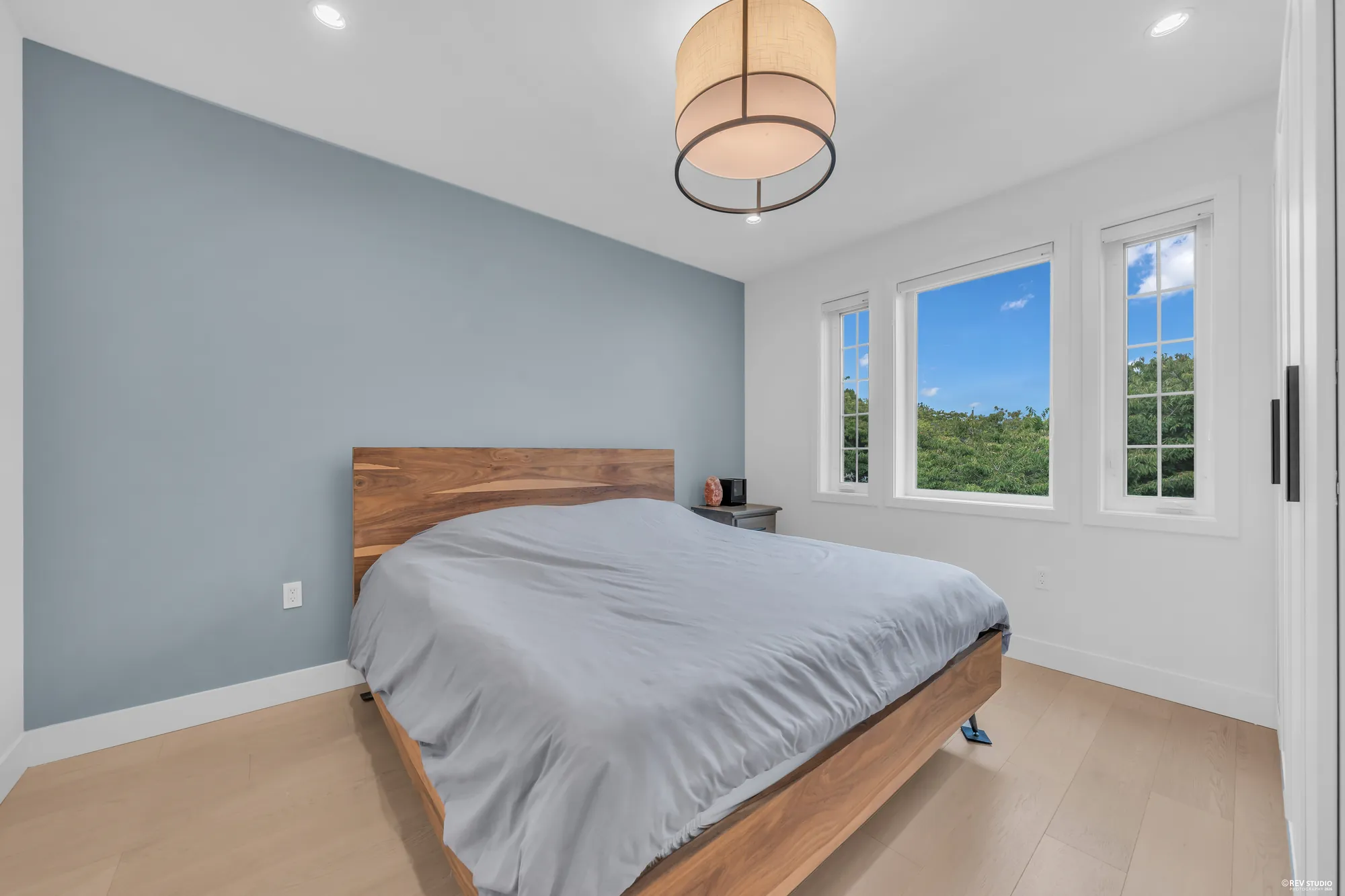 The primary bedroom: a bed against a blue-grey wall, windows on two sides