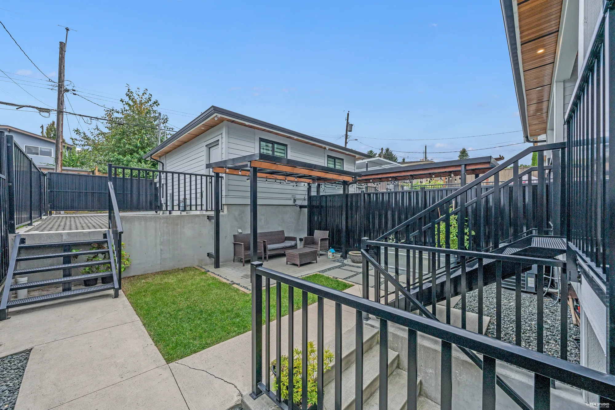 The yard below the deck: lawn and paving, the black stairs and railings, the garage beyond